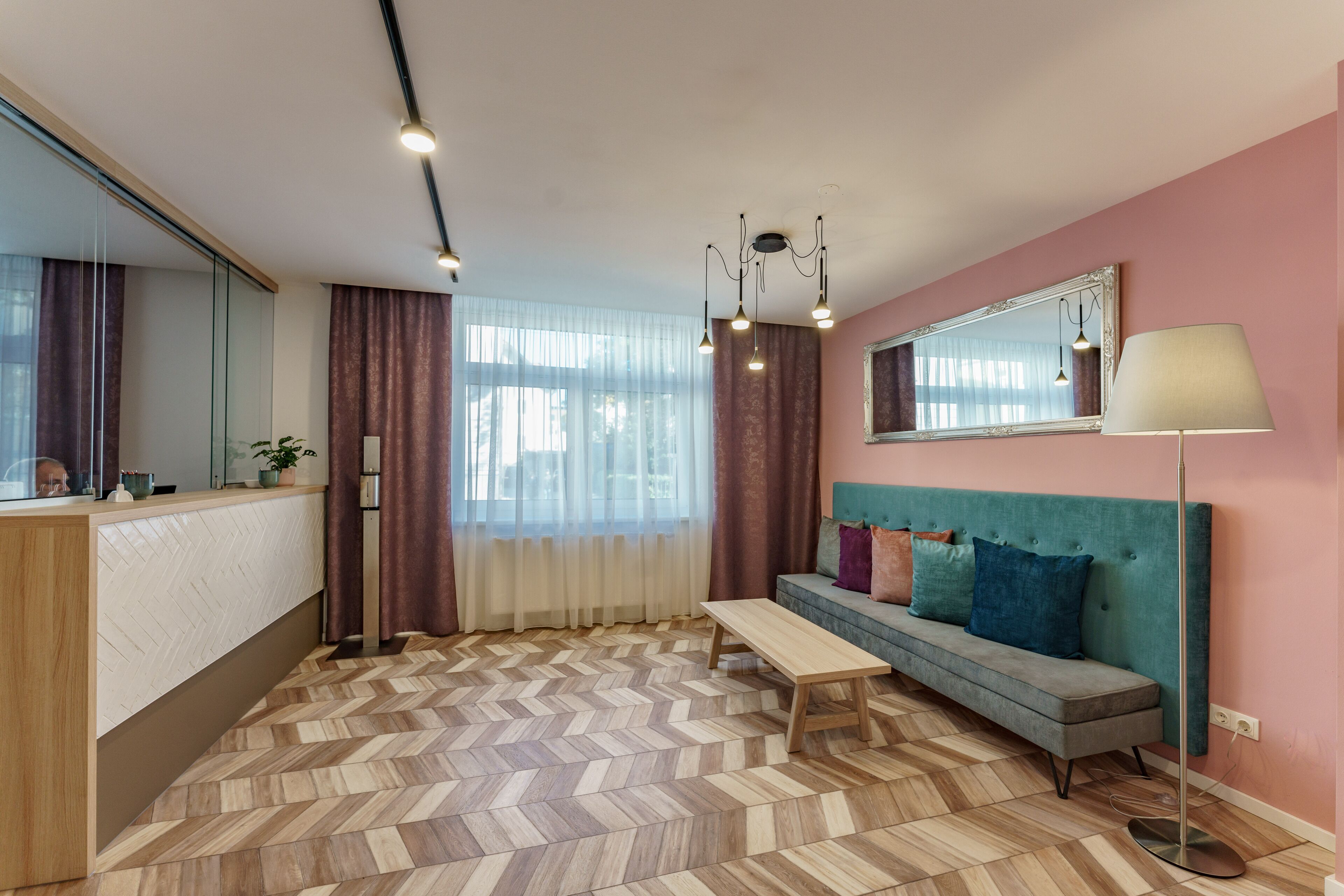 A modern living room with a herringbone floor, a sofa with cushions, a bench, a mirror, and a lamp.