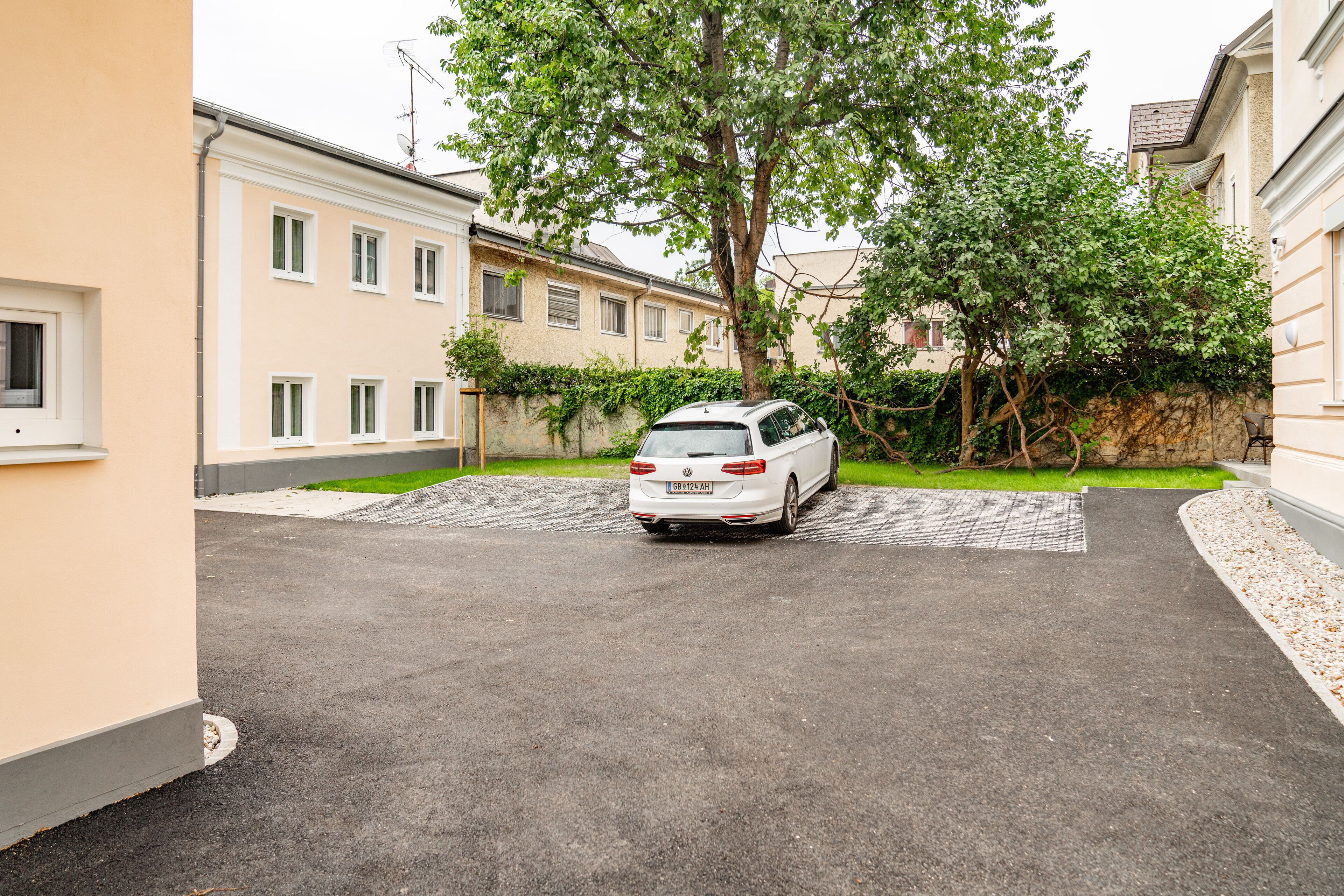 A white car parked in a driveway with a tree and a building in the background.