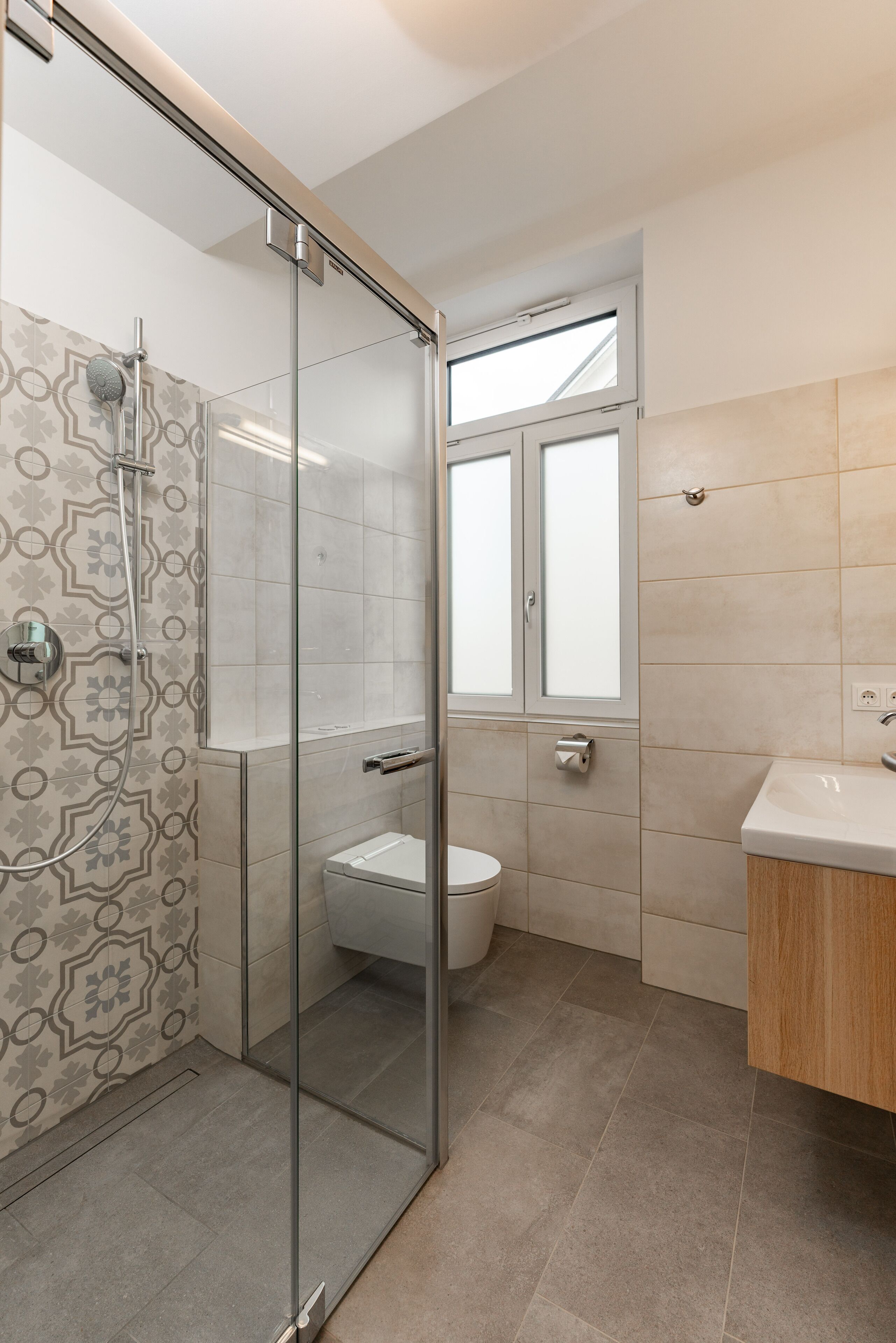 A modern bathroom with a glass shower enclosure, a toilet, and a sink with a wooden cabinet.