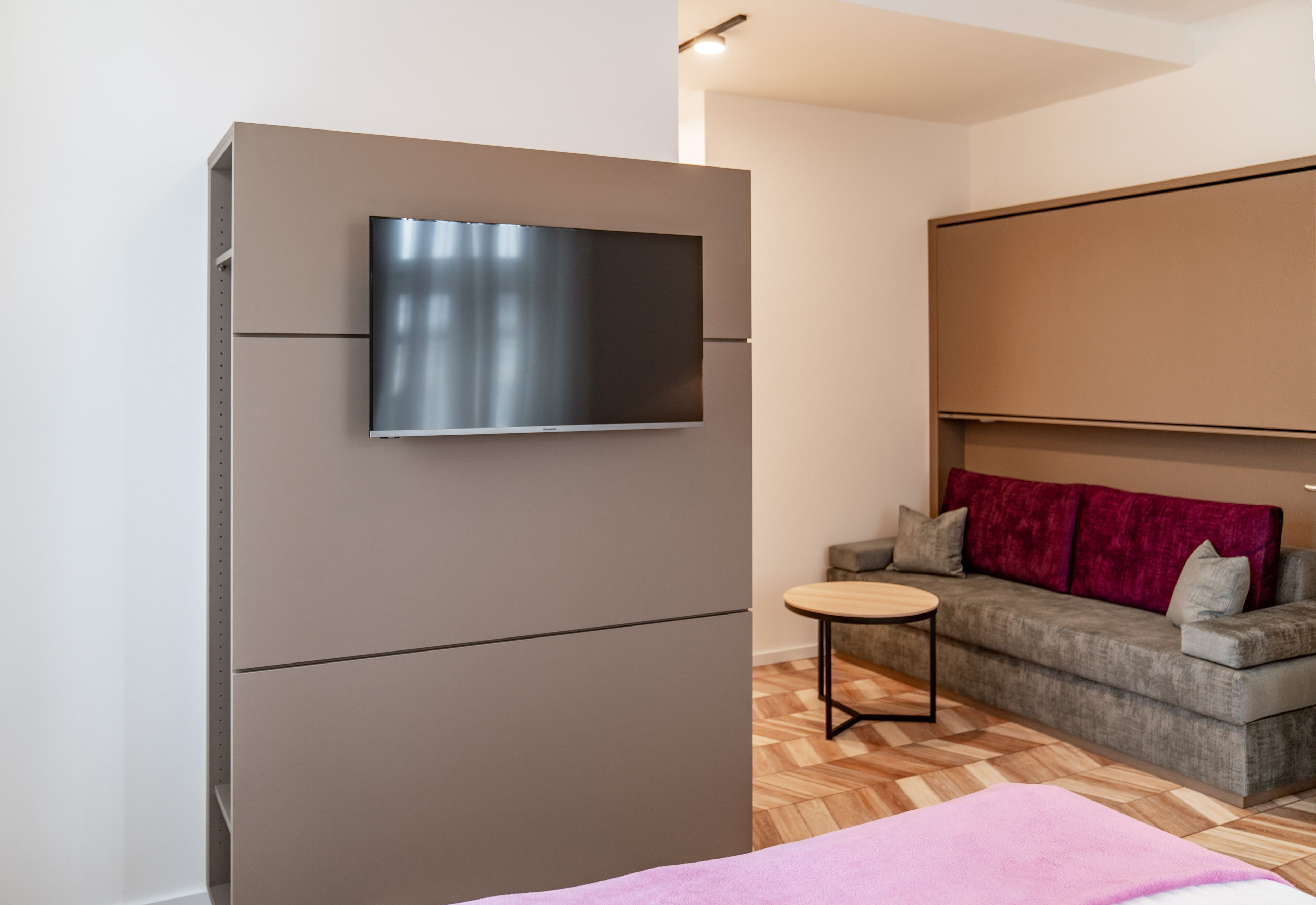 Una habitación moderna con televisión integrada, un sofá y una pequeña mesa redonda.