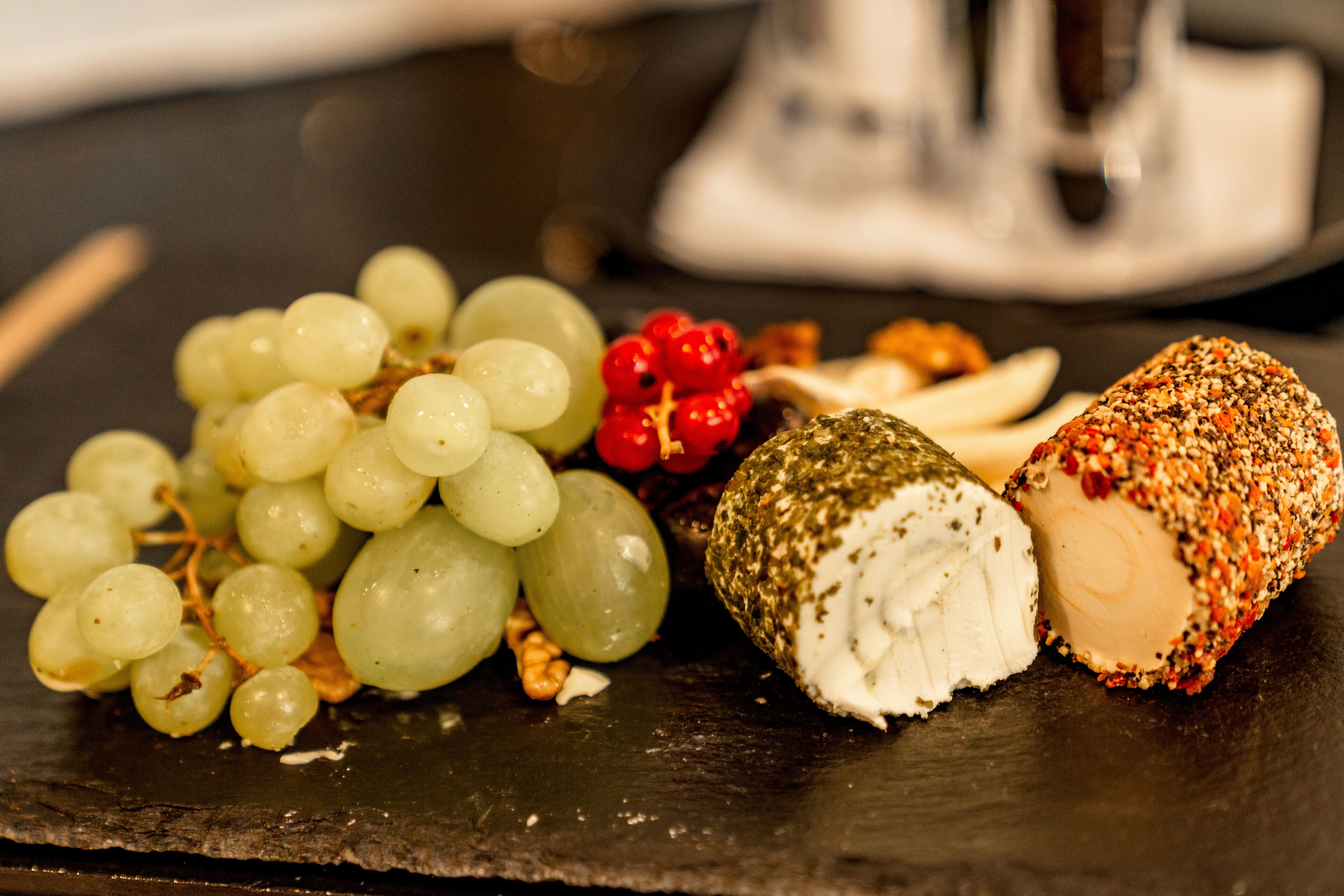 Diversos alimentos, incluindo uvas, nozes e um queijo redondo, sobre uma superfície de ardósia.