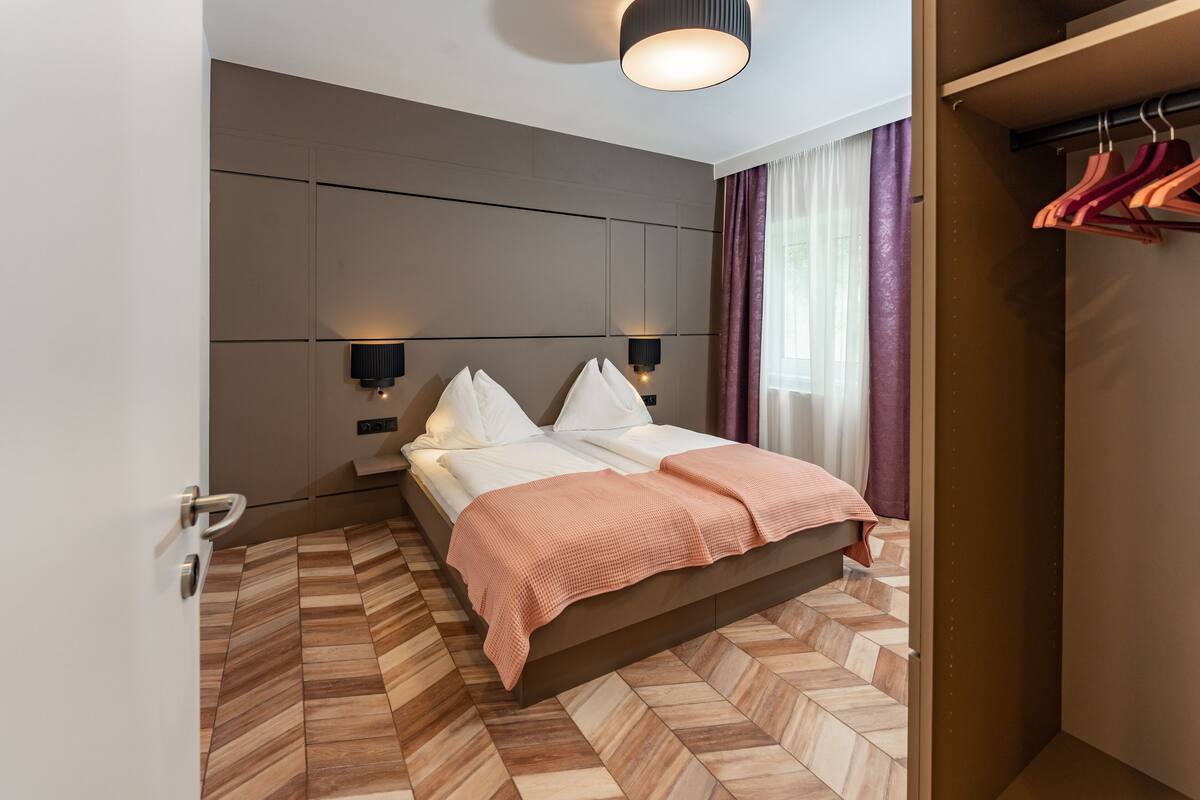 A modern hotel room with a large bed, two bedside lamps, a wardrobe, and a mirror on the wall.