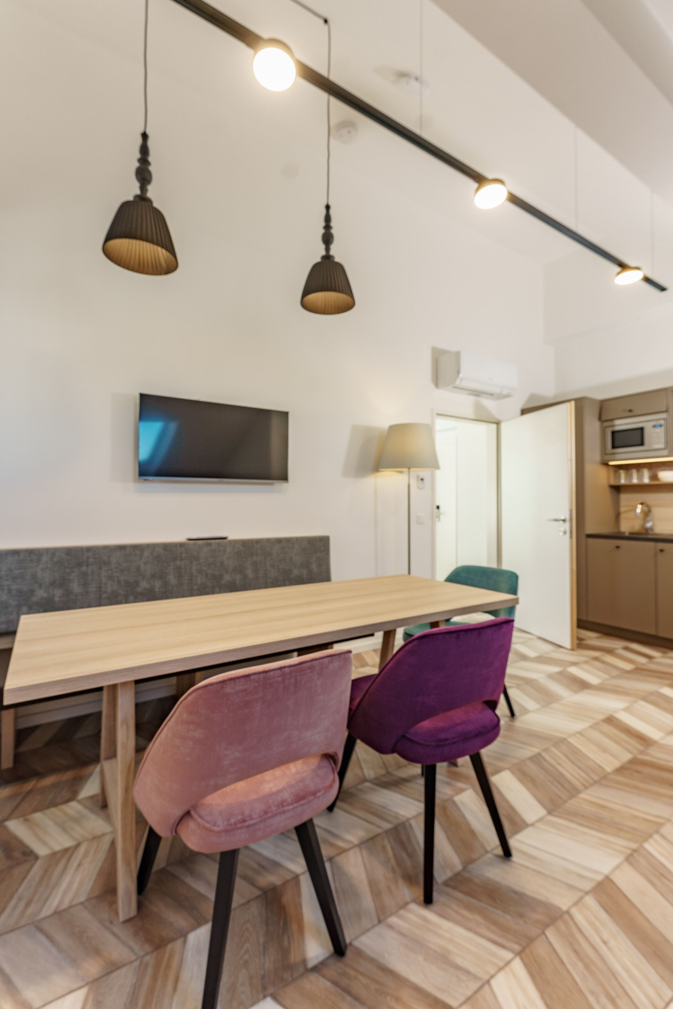 A modern dining area with a wooden table, two purple chairs, and hanging pendant lights.