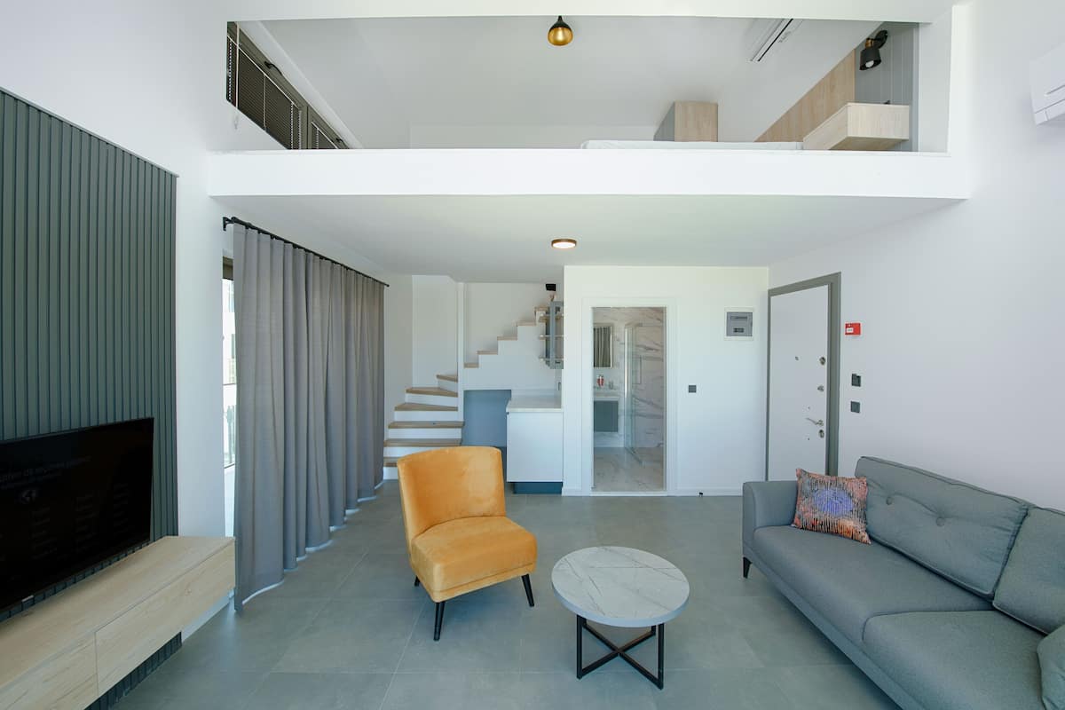 Una sala de estar moderna con un sofá, un sillón y una mesa de centro. Una escalera conduce a un nivel superior.