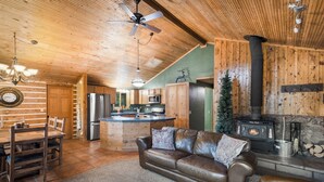 A cozy cabin interior with a wooden ceiling, a central island kitchen, a leather sofa, and a wood-burning stove. - Private Hot Tub | Mountain Retreat | ATV's | Close to Wolf Creek Ski Area (South Fork)