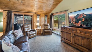 A cozy cabin interior with a leather sofa, two leather chairs, a wooden cabinet with a flat-screen TV, and a large window offering a mountain view. - Private Hot Tub | Mountain Retreat | ATV's | Close to Wolf Creek Ski Area (South Fork)