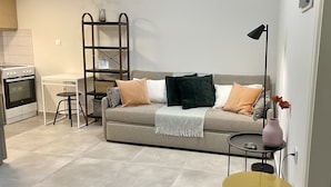 A modern living room with a sofa, a small table, a lamp, and a kitchen area with an oven.
