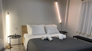 A neatly made bed with a dark quilt, white pillows, and rolled towels on a clean, tiled floor.