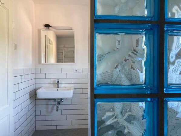 Une salle de bain avec un lavabo blanc, un miroir et un mur recouvert de carreaux.