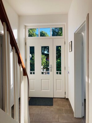 Un couloir avec une porte à deux battants, un escalier en bois et une petite fenêtre au-dessus de la porte.