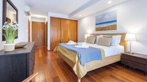 A bedroom with a bed, bedside tables, a dresser, a mirror, a potted plant, and a painting on the wall.