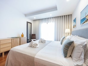 A hotel room with a bed, a desk, a chair, a mirror, and a window with curtains. - Baía da Luz Resort - Nuzone Apartment (Luz)