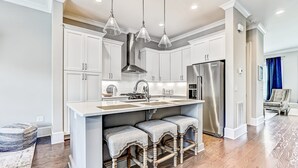 Una cocina moderna con gabinetes blancos, un refrigerador de acero inoxidable y una isla central con taburetes de bar.