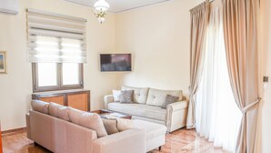 Una sala de estar con un sofá color beige, un sofá más pequeño, un televisor y una ventana con persianas.