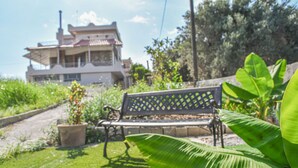 Un banco en un jardín con una casa al fondo.