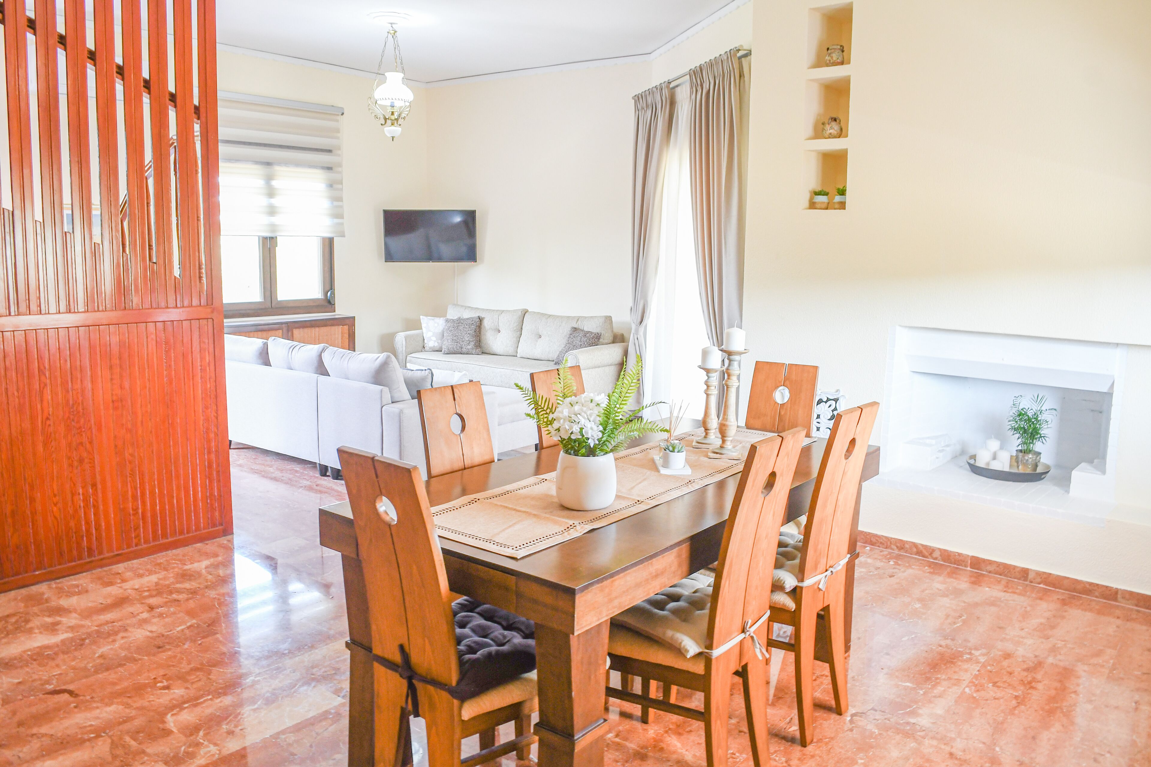 A dining area with a wooden table and chairs, a sofa in the background, and a fireplace.