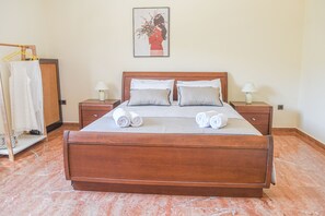 Un letto ben rifatto con cuscini e asciugamani arrotolati, una testiera in legno e due comodini con lampade.
