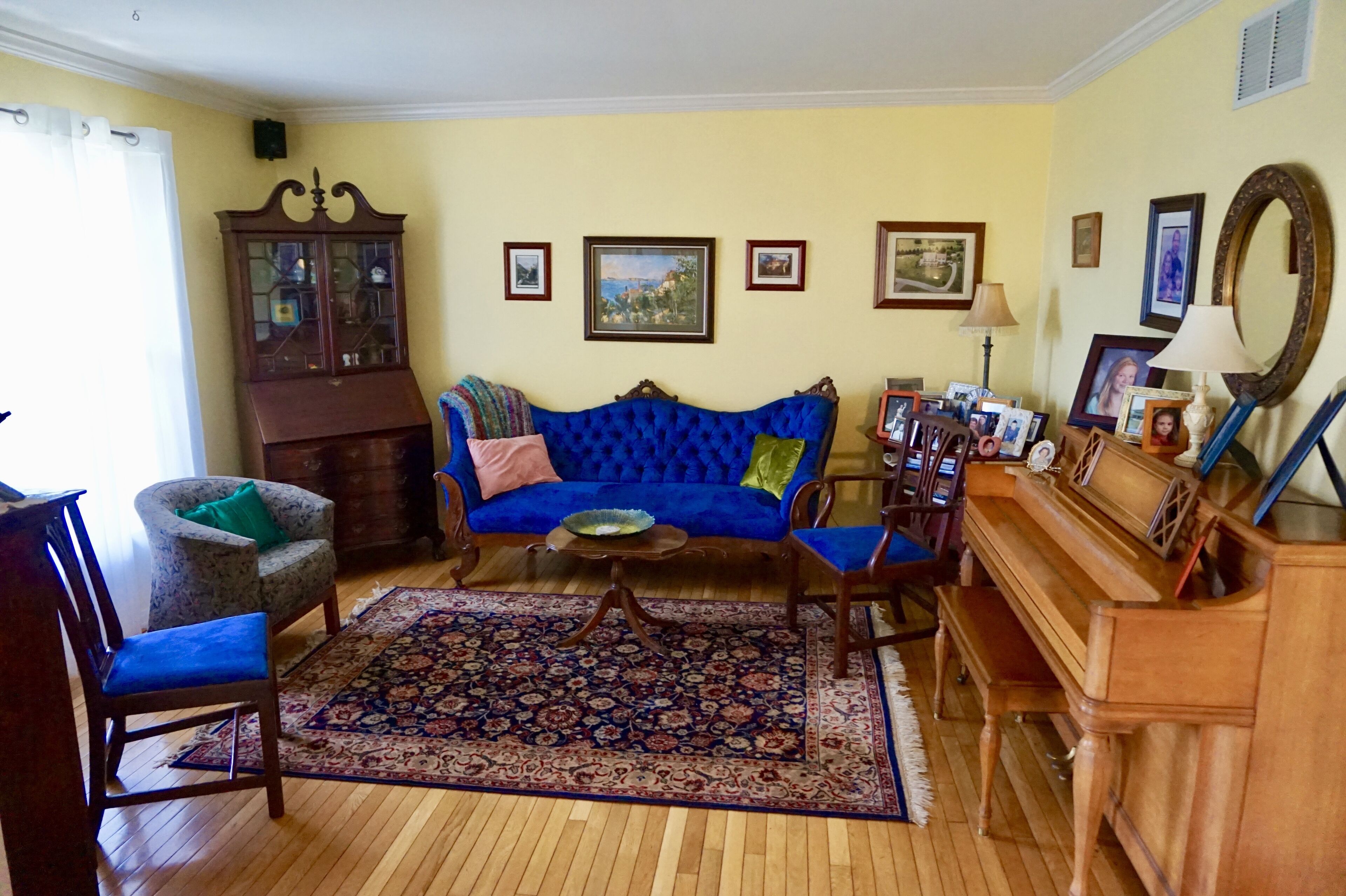 A living room with a blue sofa, a wooden cabinet, a piano, and a patterned rug.