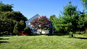 Une maison blanche avec un toit bleu, entourée d’herbe verte et d’arbres.