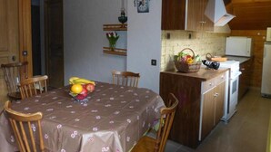 Un comedor con una mesa dispuesta para cuatro personas, una cocina con armarios de madera y un reloj en la pared.