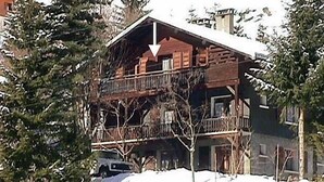 Una cabaña de madera con balcón, rodeada de nieve y árboles.