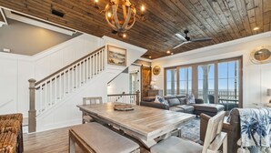 A spacious living area with a wooden ceiling, a dining table with benches, a sofa, and a large window offering a view.