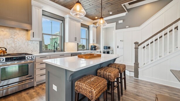 A modern kitchen with a large island, stainless steel appliances, and a herringbone tile backsplash.
