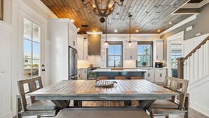 A spacious kitchen with a large wooden table, white cabinetry, and a wooden ceiling.