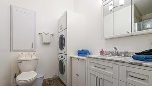 A compact bathroom with a toilet, washing machine, and sink with a mirror above. - Newly Remodeled Studio w/ AC & Private Entrance (Port Angeles)