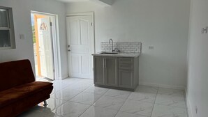 Amplia sala de estar con sofá, cocina con salpicadero de azulejos y puerta que da a otra habitación.