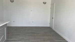 Een kamer met een grijze betegelde vloer, witte muren en een deur aan de rechterkant.