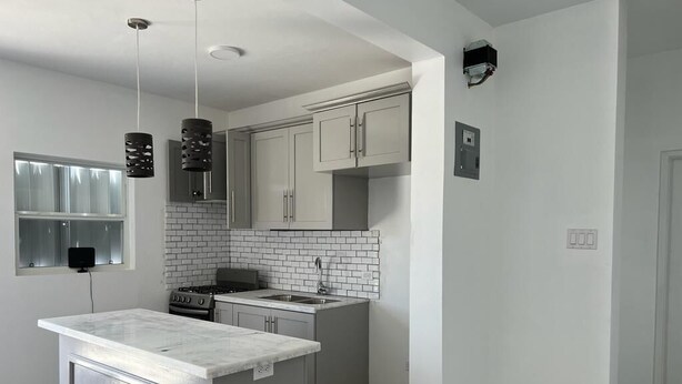Una cocina moderna con armarios grises, una isla blanca y lámparas colgantes negras.