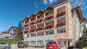 A multi-story hotel with balconies adorned with flowers, a clear sky, and parked cars in the foreground. - 'Residence Diana Apartment 101' with Mountain View, Balcony & Wi-Fi (Terenten)