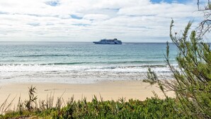 A beach with a cruise ship in the distance, clear skies, and ocean waves.