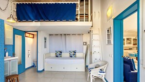 A compact room with a bunk bed, a small seating area, and a kitchenette.