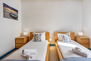 A hotel room with two beds, wooden headboards, nightstands with lamps, and a painting of a boat on the wall.