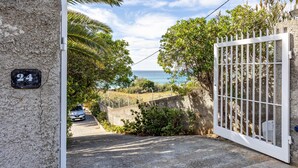 A gated entrance with a view of the sea, a number sign, and a parked car.