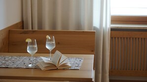 Een houten bank met een geweven onderzetter, twee glaasjes water met citroenpartjes en een open boek.