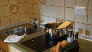 Een keuken met een spoelbak, kookplaat en diverse kookgerei.