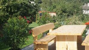 Een houten picknicktafel en bank in een tuin met potplanten en een speeltuin op de achtergrond.