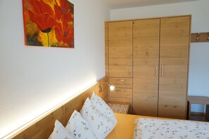 A bedroom with a wooden wardrobe, a bed with floral bedding, and a wall-mounted lamp.