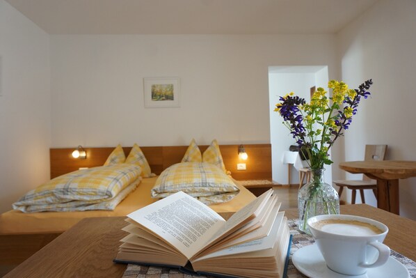 Une chambre d’hôtel avec un lit, une table sur laquelle est posé un livre ouvert et une tasse de café, et un vase rempli de fleurs.