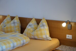 Un lit avec une couvre-lit à carreaux jaunes et blancs, une tête de lit en bois et un luminaire fixé au mur.