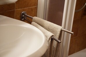 Une salle de bain avec un lavabo blanc, un porte-serviettes sur lequel est posée une serviette beige, et des murs recouverts de carreaux marron.