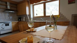 Eine Küche mit Holzschnitzereien, einem Fenster, einer Arbeitsplatte, einem Tisch mit Platzdeckchen, einer Vase mit Blumen und einem Teller mit Speisen.