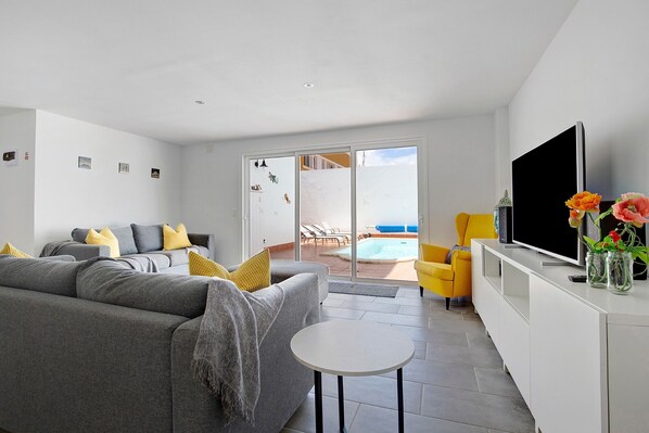 A modern living room with a grey sofa, a small white table, a flat-screen TV, and a yellow armchair.