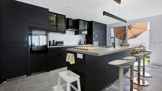 A modern kitchen with dark cabinetry, a central island, and a bar area with stools. - 'Villa Pacifica' with heated pool, terrace, lounge area & Wi-Fi (Corralejo)
