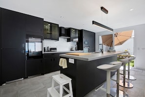 A modern kitchen with dark cabinetry, a central island, and a bar area with stools.
