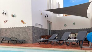 A poolside area with lounge chairs, a shaded umbrella, and decorative wall elements. - 'Villa Pacifica' with heated pool, terrace, lounge area & Wi-Fi (Corralejo)