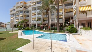 Ein Hotel mit Swimmingpool, Palmen und Balkonen mit gelben Markisen.